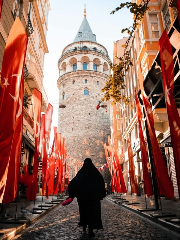 pexels photo 15850737 15850737 A silhouette of a person walking towards the iconic Galata Tower in Istanbul adorned with Turkish flags.